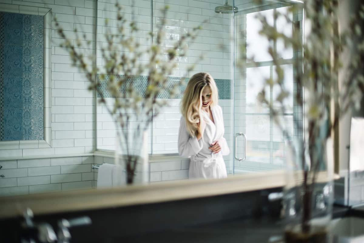 A bathroom with a large mirror, white tiles, and a vase with flowers.