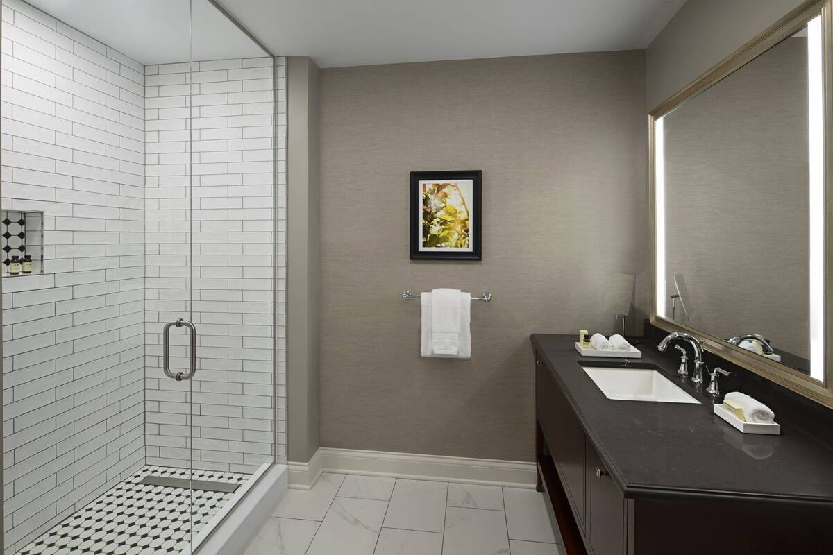 A modern bathroom with a shower, two sinks, a large mirror, and a framed picture on the wall.