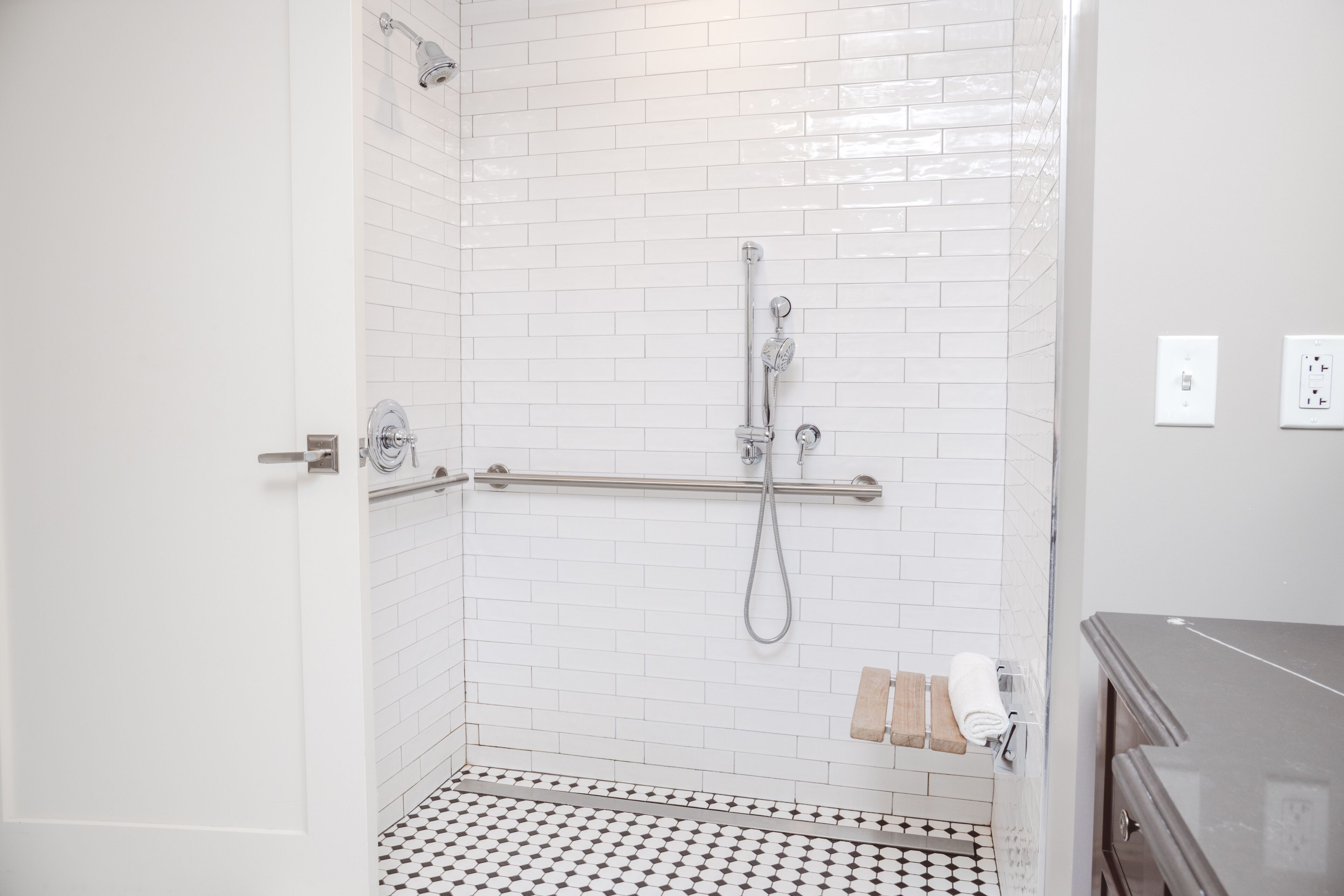 A bathroom with white tiled walls, a shower with a grab bar, a toilet, and a sink.
