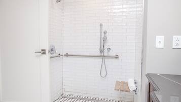 A bathroom with white tiled walls, a shower with a grab bar, a toilet, and a sink.