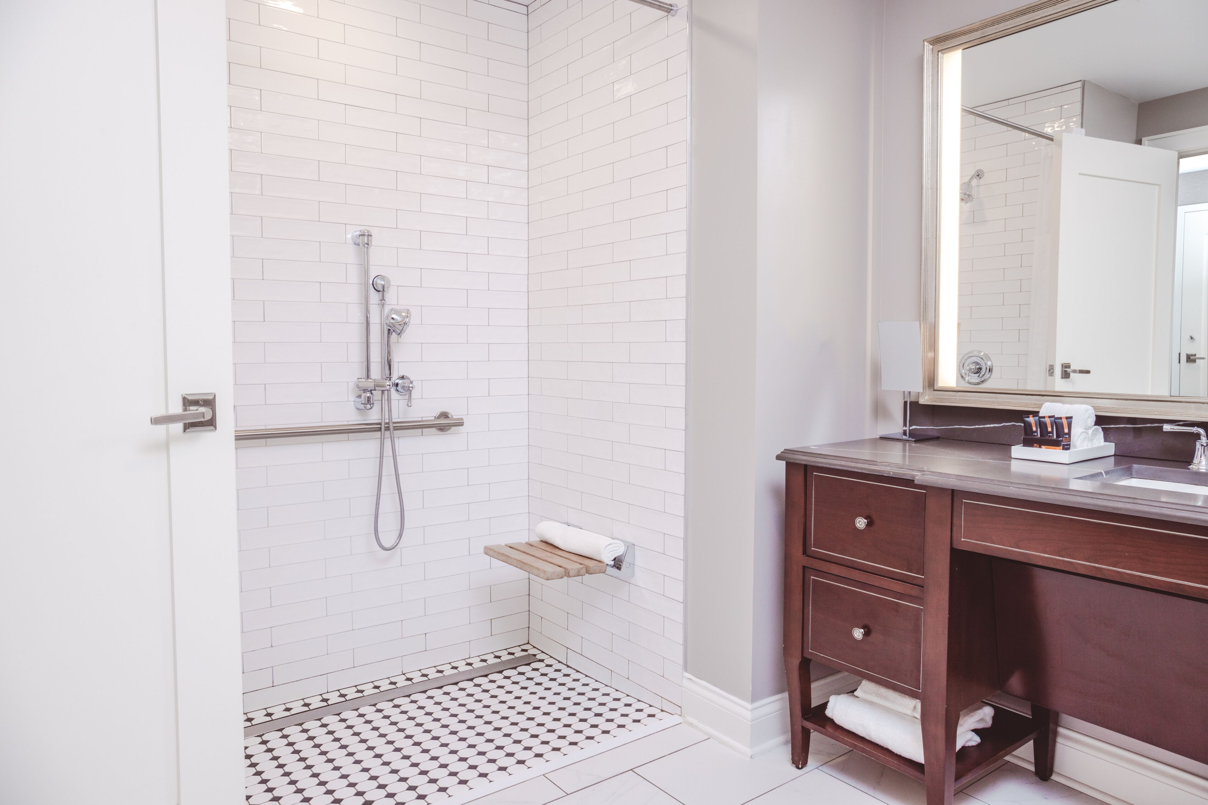 A bathroom with a shower, a wooden shelf, a vanity with a mirror, and a towel rack.