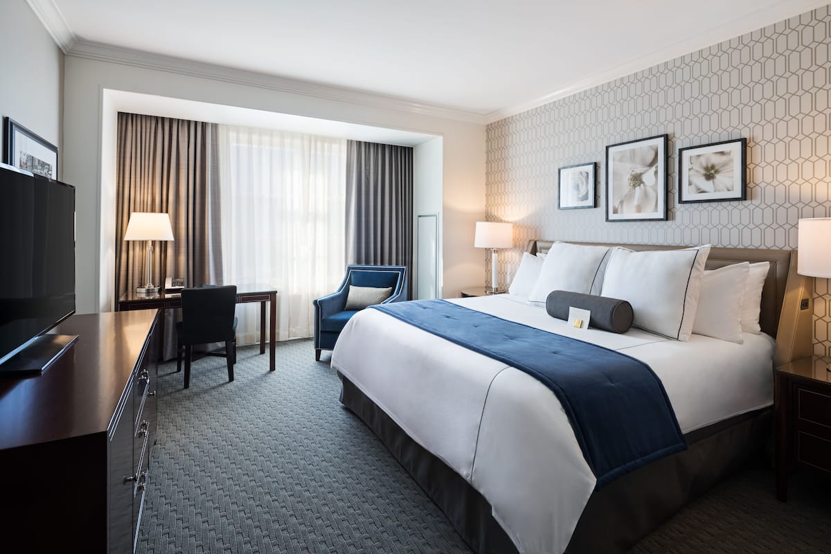 A hotel room with a large bed, a desk with a chair, a TV, and a window with curtains.