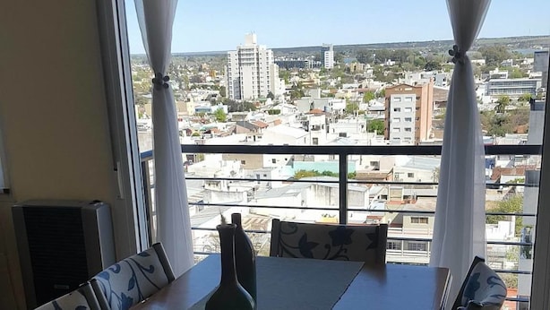 A dining area with a table and chairs, a vase, and a view of a cityscape through large windows.
