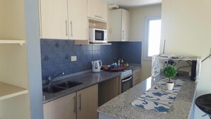 A compact kitchen with a microwave, stove, sink, and a small potted plant.