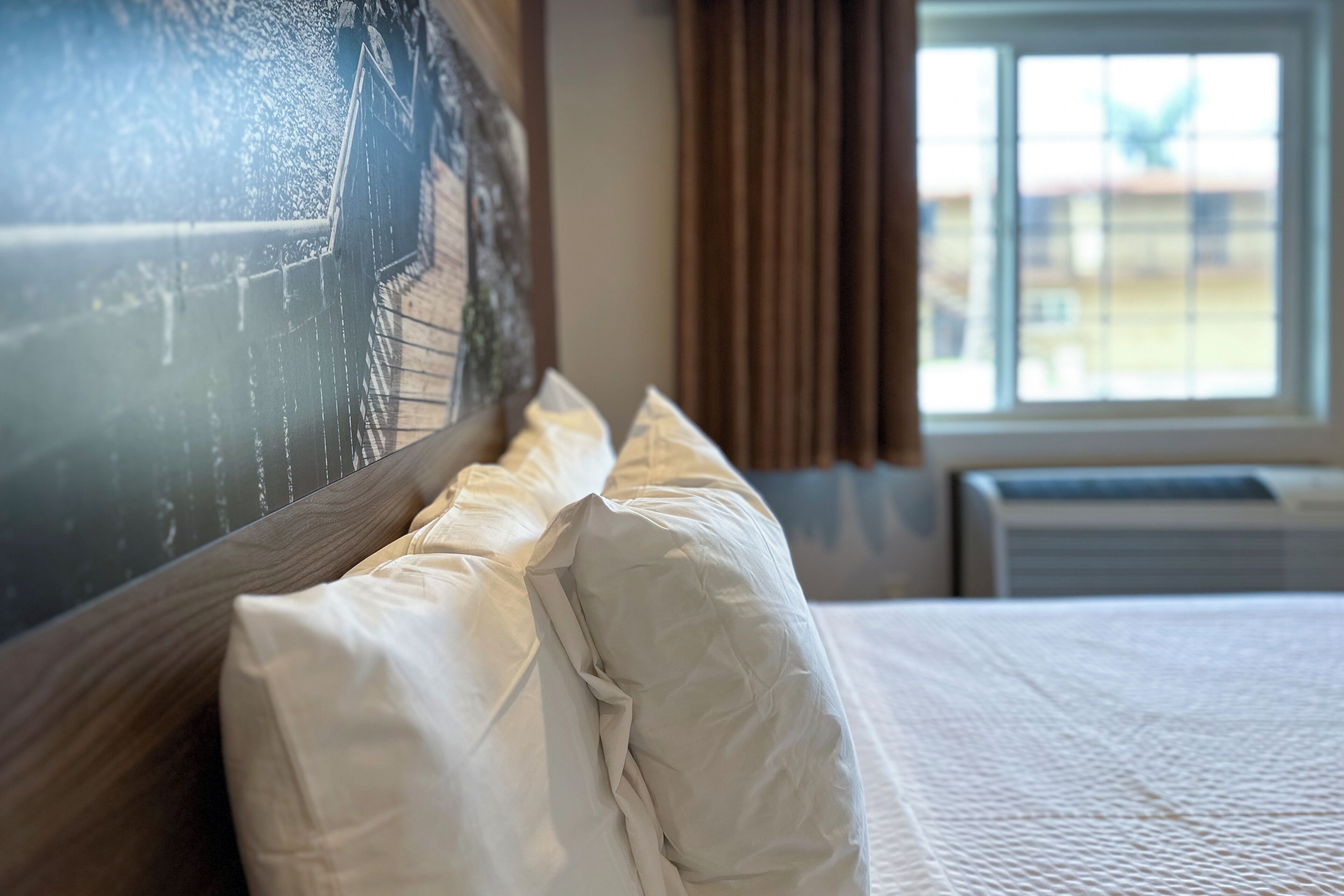 Habitación de hotel con una cama grande, cabecera con un mural de paisaje urbano, ventana con cortinas y un equipo de aire acondicionado.
