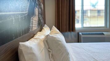 Habitación de hotel con una cama grande, cabecera con un mural de paisaje urbano, ventana con cortinas y un equipo de aire acondicionado.
