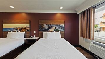 Quarto de hotel com duas camas, um quadro grande na parede, uma mesa de cabeceira e uma janela com cortinas.