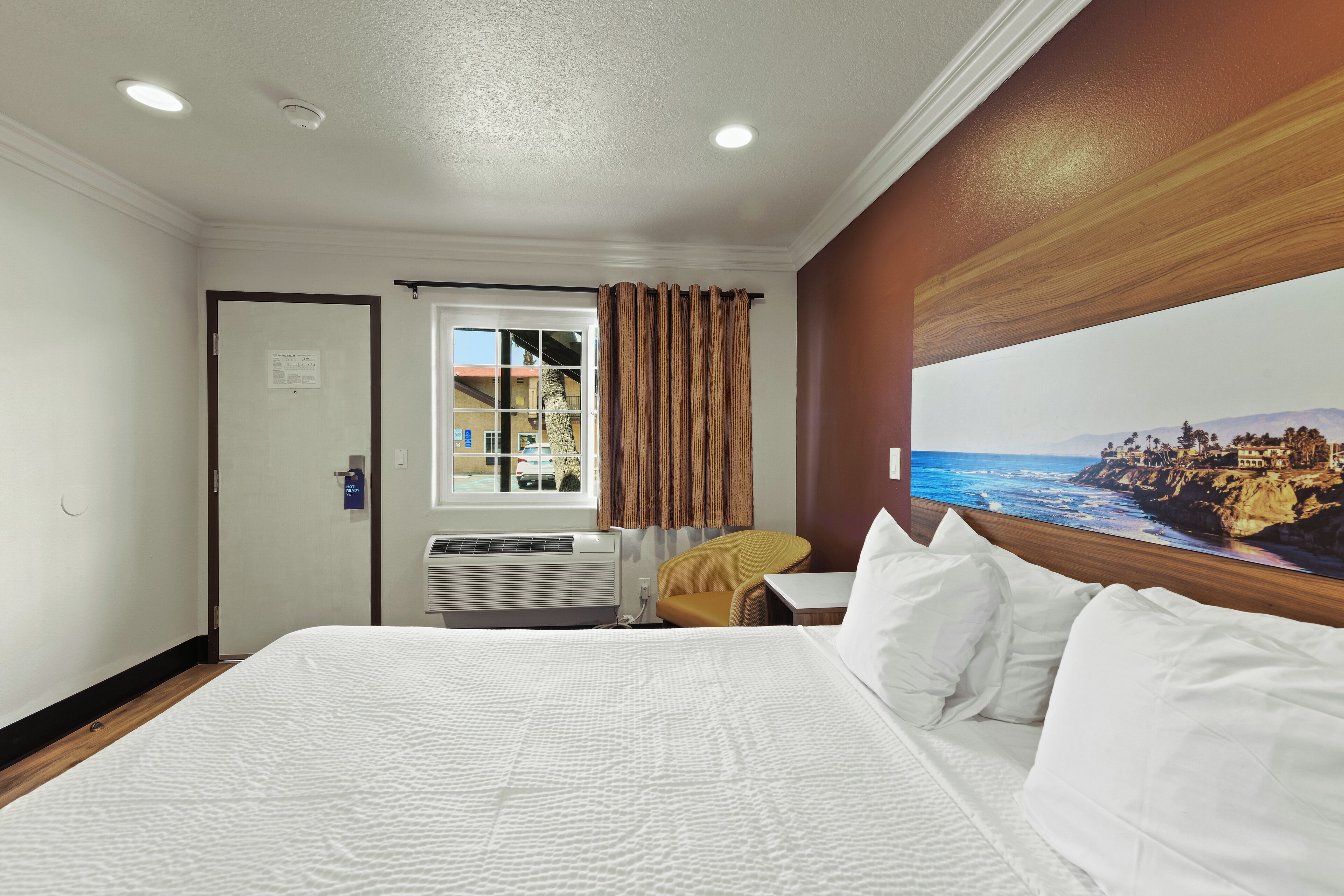 Habitación de hotel con una cama grande, una ventana con cortinas, una silla y vistas a un paisaje costero.
