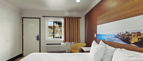 Habitación de hotel con una cama grande, una ventana con cortinas, una silla y vistas a un paisaje costero.
