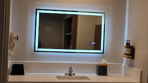 A bathroom with a large mirror, a sink, a towel rack, and a soap dispenser.