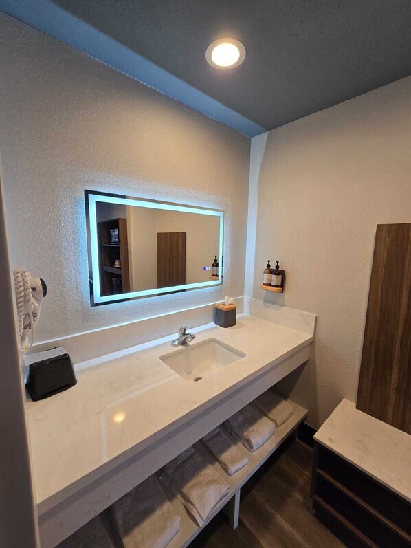 A modern bathroom with a white sink, a mirror with a backlight, a towel rack, and a wooden door.