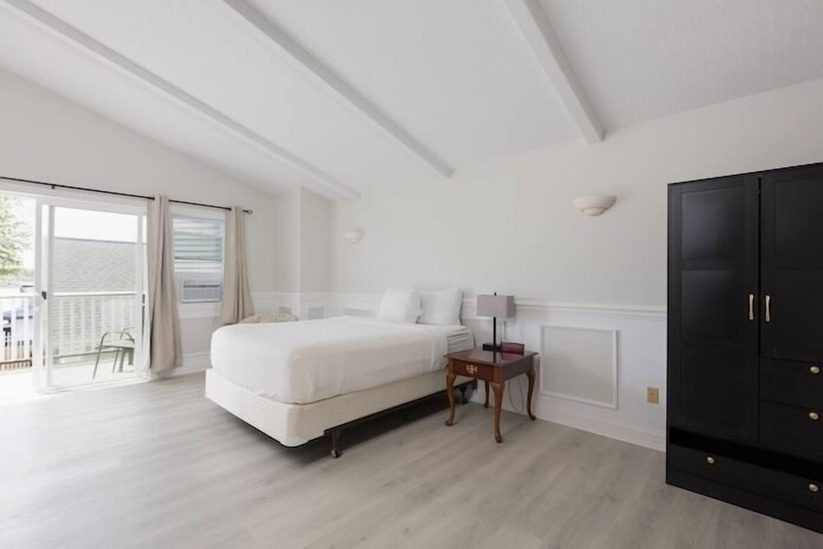 A bedroom with a bed, a nightstand, a lamp, a wardrobe, and a sliding glass door leading to an outdoor area.