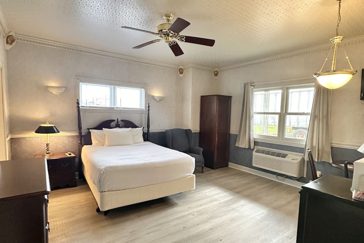 A spacious bedroom with a large bed, a ceiling fan, a window with curtains, and a radiator.