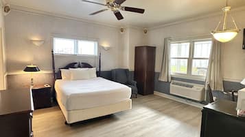 Une chambre spacieuse avec un grand lit, un ventilateur de plafond, une fenêtre avec des rideaux et un radiateur.