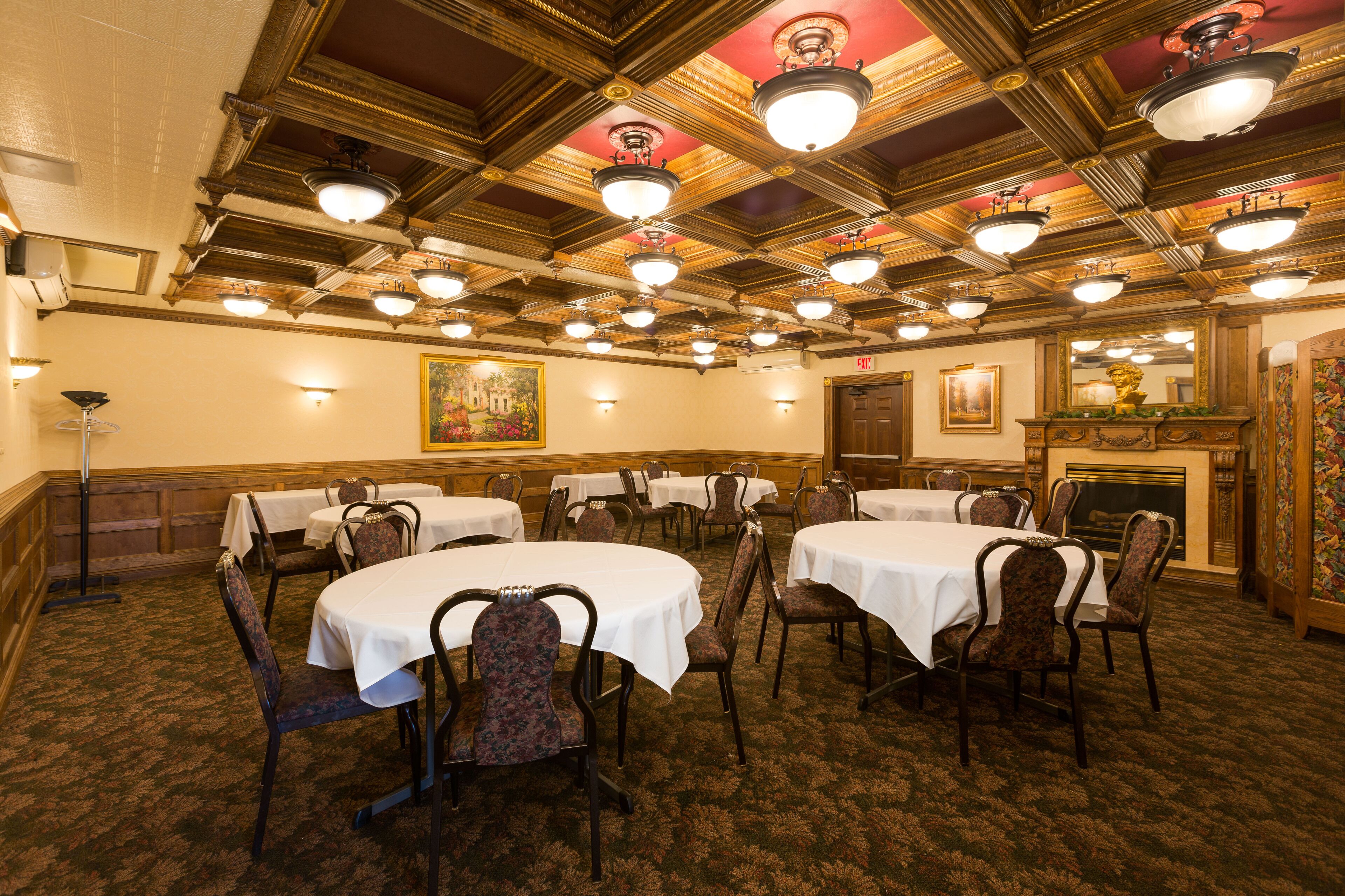 A banquet hall with round tables and chairs, ornate ceiling, and a fireplace.