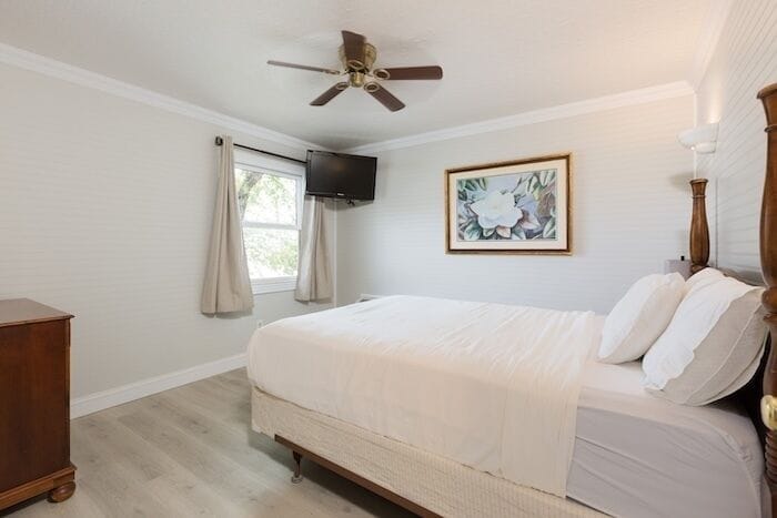 A bedroom with a bed, a ceiling fan, a television, a window with curtains, and a framed picture on the wall.