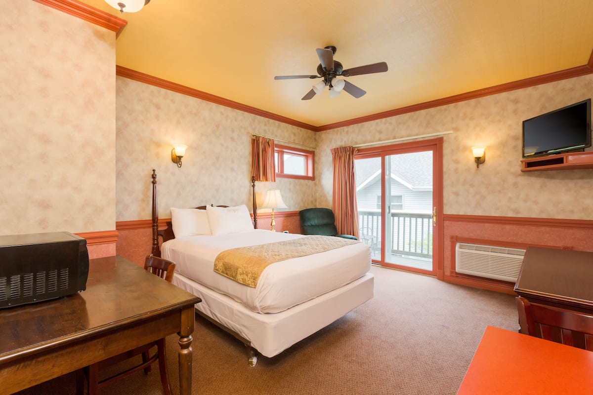 A hotel room with a bed, a desk, a chair, a television, and a balcony.