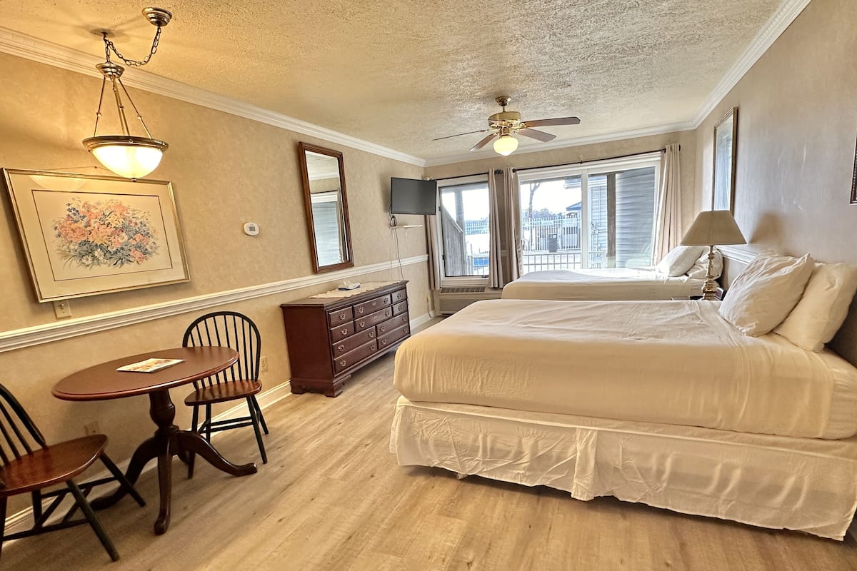 A bedroom with a large bed, a dresser, a chair, a table, and a ceiling fan.