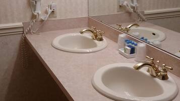 A bathroom with two sinks, each with a gold faucet, and a hairdryer mounted on the wall.