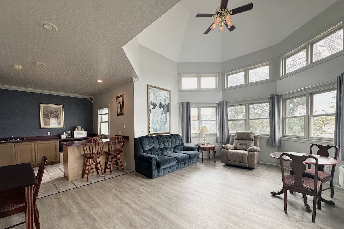 A spacious living area with a kitchen, a dark blue sofa, a beige armchair, and a dining table with chairs.