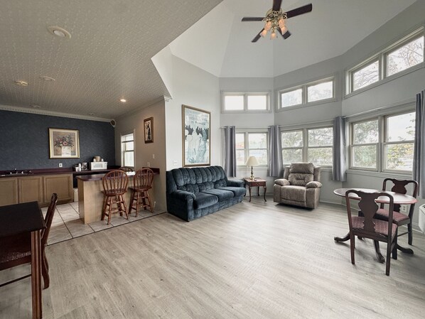 A spacious living area with a kitchen, a dark blue sofa, a beige armchair, and a dining table with chairs.