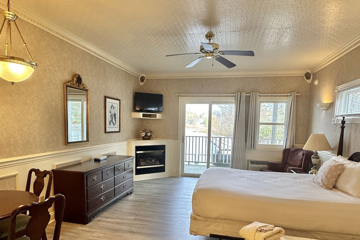 A spacious room with a large bed, a sitting area with a table and chairs, a fireplace, and a view through a sliding glass door.