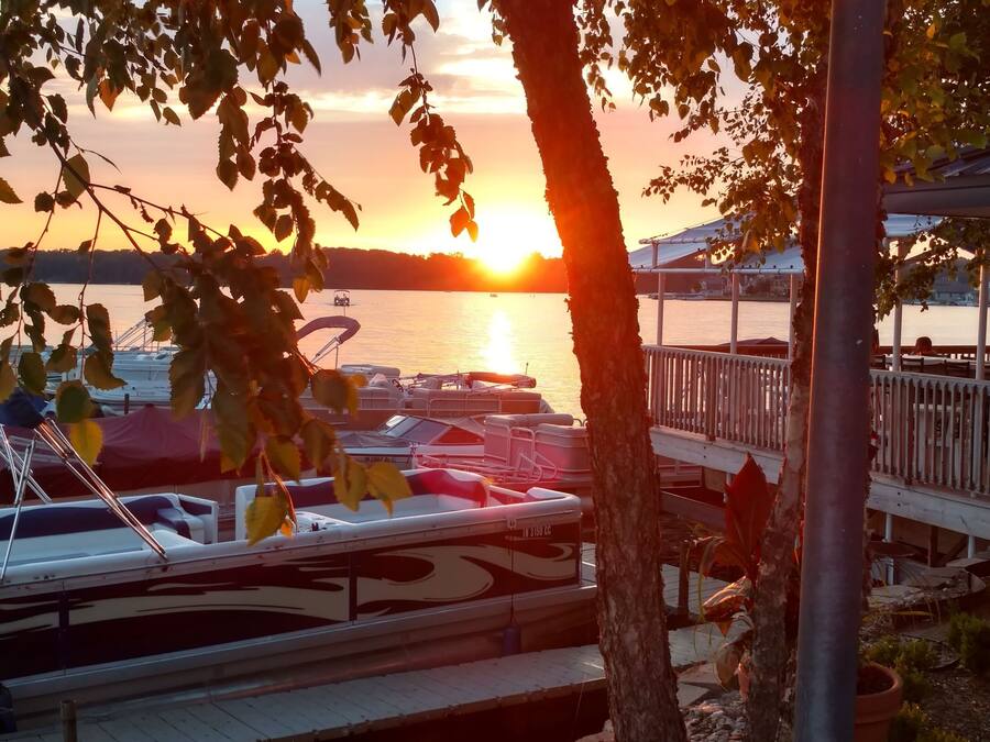 Vista al frente del agua con barcos amarrados, un muelle y el sol poniéndose al fondo.