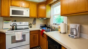 A kitchen with wooden cabinets, a white microwave, a stove, a sink, and a coffee maker.