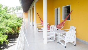 A yellow building with white columns and a covered balcony. There are white chairs and tables, and red hammocks hanging from the columns. - Pousada Recanto Rubaiyat (Ipojuca)