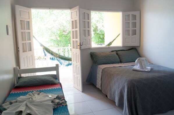 Quarto com duas camas, uma rede e vista para o verde lá fora.