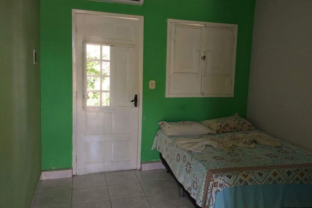 Habitació amb una paret verda, una porta blanca i un llit amb un edredó estampat.