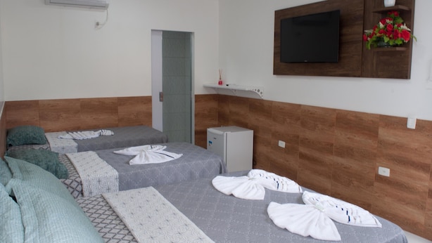 A hotel room with two beds, a TV mounted on the wall, a small refrigerator, and a flower arrangement on a shelf. - Pousada Recanto Rubaiyat (Ipojuca)