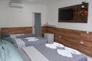 A hotel room with two beds, a TV mounted on the wall, a small refrigerator, and a flower arrangement on a shelf. - Pousada Recanto Rubaiyat (Ipojuca)