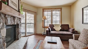 A living room with a stone fireplace, a brown leather sofa, a patterned armchair, and a coffee table. - 8493 Dakota Lodge (Keystone)