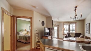 A spacious kitchen with a dishwasher, a dining area with a table and chairs, a living room with a sofa and a television, and a bedroom with a bed and a lamp. - 8493 Dakota Lodge (Keystone)