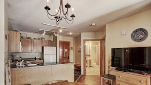 A kitchen with wooden cabinets, a refrigerator, a chandelier, a dining table, and a television. - 8493 Dakota Lodge (Keystone)