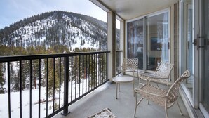 Un balcón con vistas a montañas nevadas, mobiliario de mimbre y una puerta de cristal.