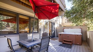 A deck with a table and chairs, a hot tub, and a red umbrella.