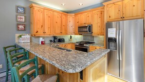 A kitchen with wooden cabinets, a granite countertop, a stainless steel refrigerator, and a built-in stove.
