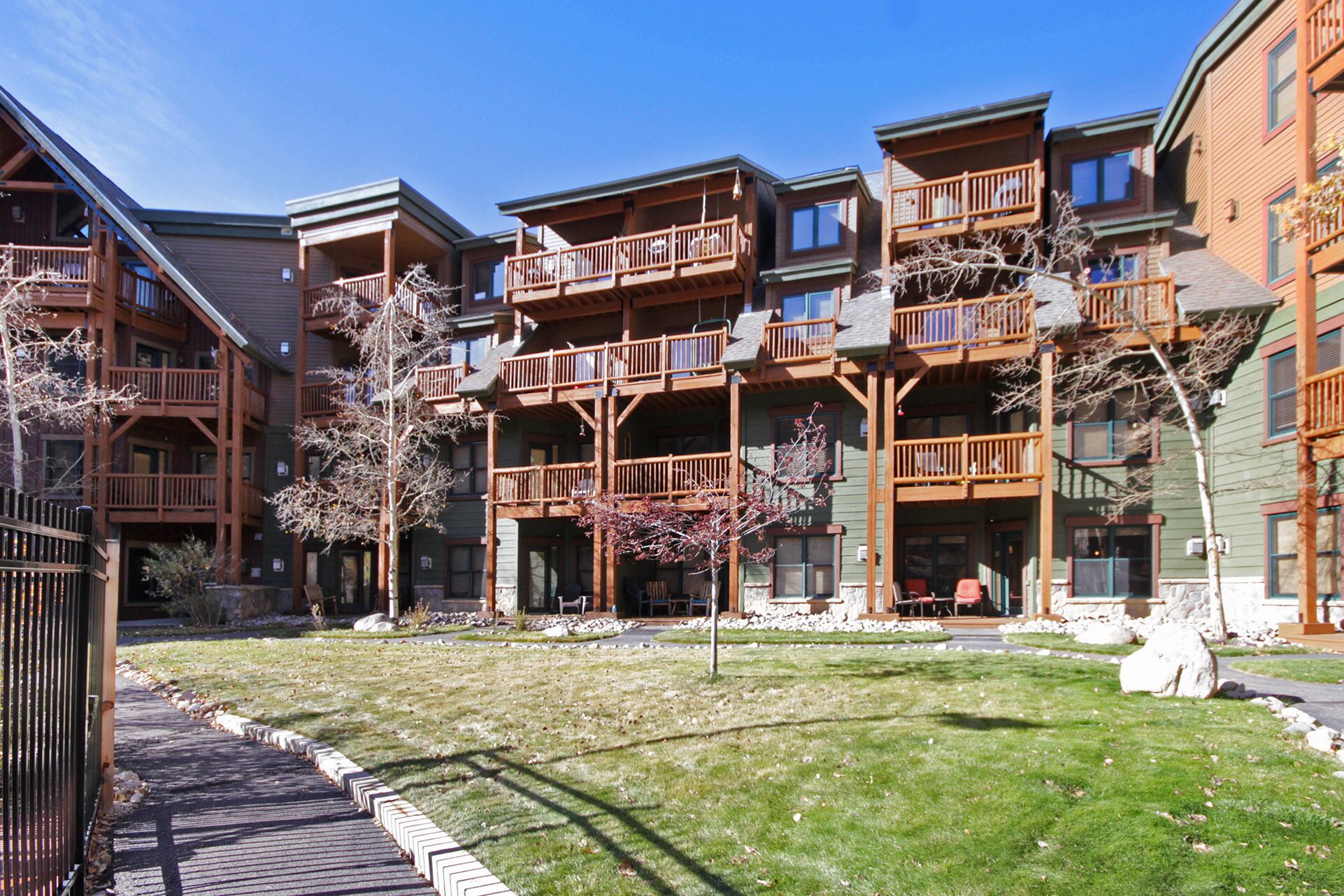 A multi-story building with balconies, a grassy courtyard, and a stone pathway.
