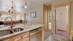 A kitchen with granite countertops, stainless steel sink, wooden cabinets, and a chandelier. - 2609 Tenderfoot Lodge (Keystone)