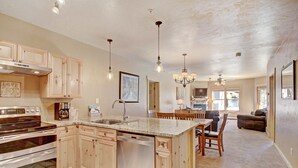 A spacious kitchen with granite countertops, wooden cabinets, and stainless steel appliances. There is a dining area with a table and chairs, and a living room with a sofa and a television. - 2609 Tenderfoot Lodge (Keystone)