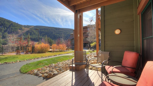 A wooden deck with outdoor seating, a view of a mountain, and a building with a green exterior. - 2609 Tenderfoot Lodge (Keystone)