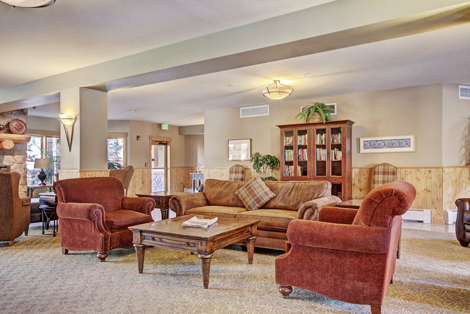 A spacious lobby with a wooden floor, a brown leather sofa set, a wooden coffee table, and a large wooden cabinet with books.