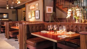 A restaurant with wooden booths and tables, each with a set of wine glasses and cutlery. - Hotel Clermont (Atlanta)
