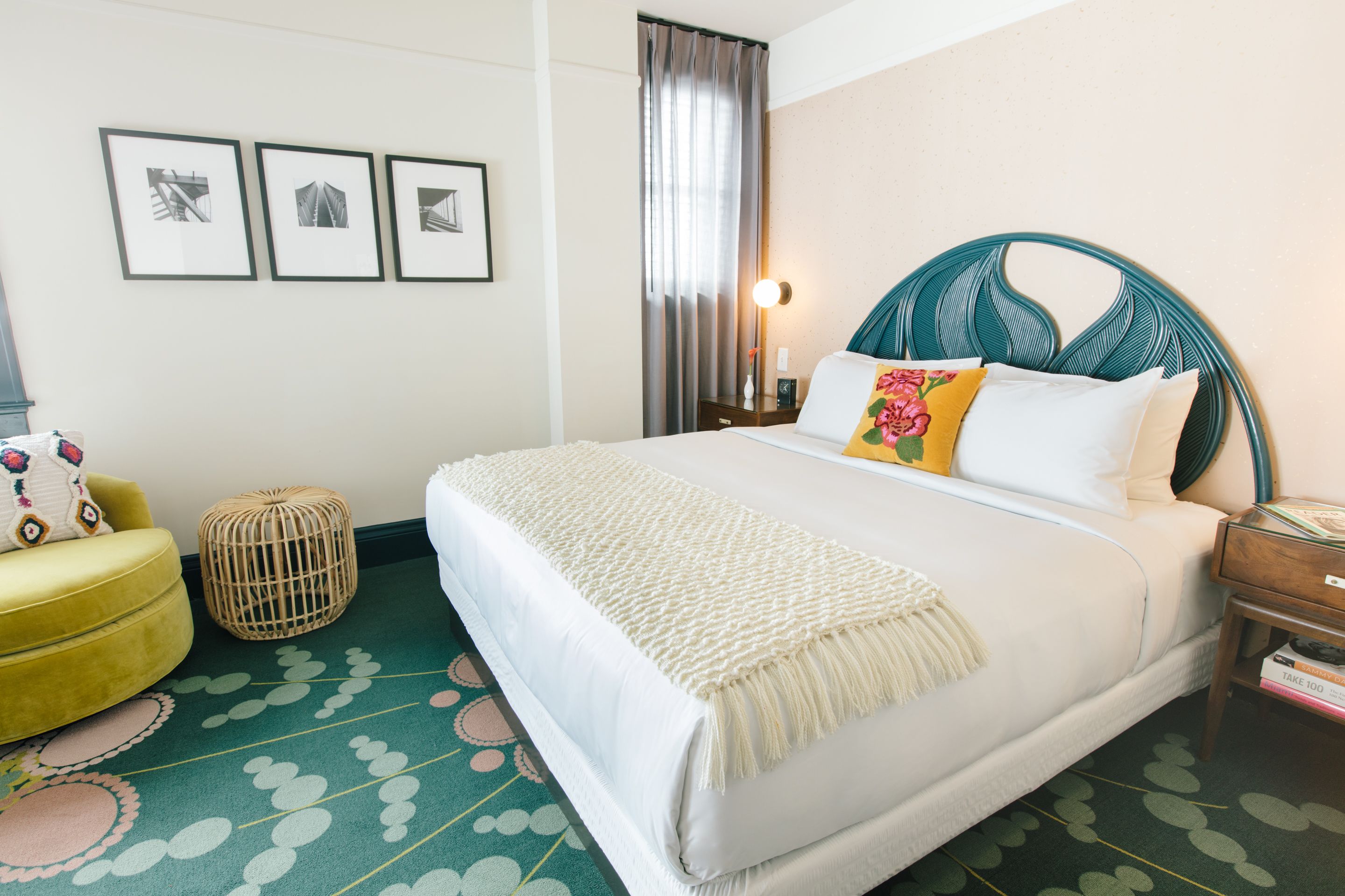 Ein ordentlich eingerichtetes Hotelzimmer mit einem großen Bett, einem kleinen runden Hocker, einem gelben Sessel und einem Nachttisch mit Lampe.
