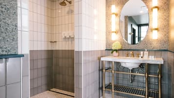 A bathroom with a shower, a sink with a marble countertop, and a mirror with wall sconces.