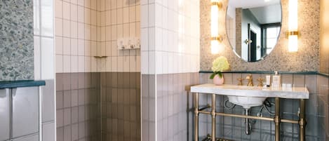 A bathroom with a shower, a sink with a marble countertop, and a mirror with wall sconces.