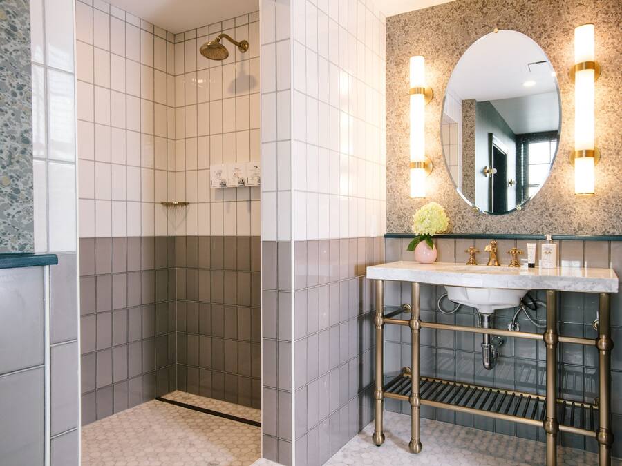 A bathroom with a shower, a sink with a marble countertop, and a mirror with wall sconces.