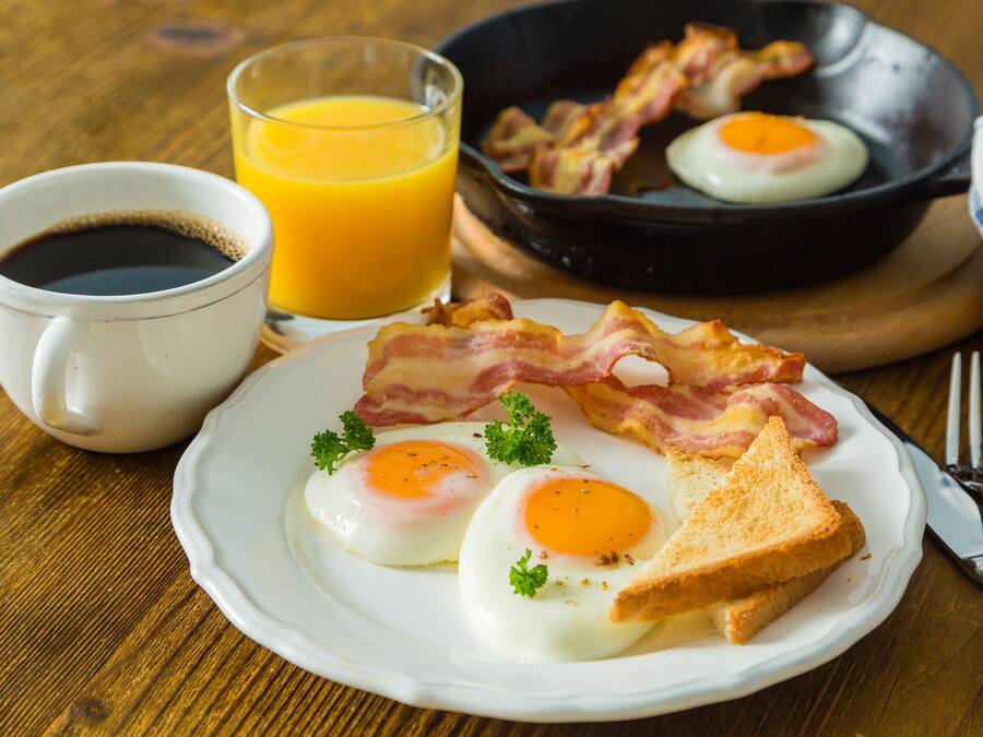 A breakfast plate with eggs, bacon, toast, and a cup of coffee.